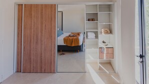 A modern hotel room with a wooden sliding door, a neatly made bed, a small bedside table, and a built-in wardrobe with shelves.