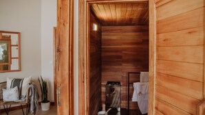A wooden sauna room with a bench, a potted plant, and a towel rack.