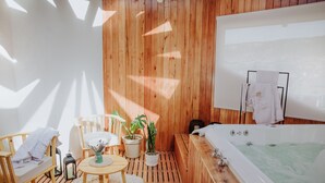 A wooden-paneled room with a bathtub, a small table with chairs, a potted plant, and a white rug.
