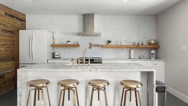 Una cocina moderna con una isla de mármol, electrodomésticos de acero inoxidable y taburetes de barra dorados.