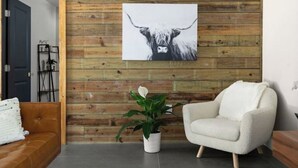 Una habitación con pared de madera, un sillón blanco, una planta en maceta y un cuadro con la imagen de una cabeza de toro.