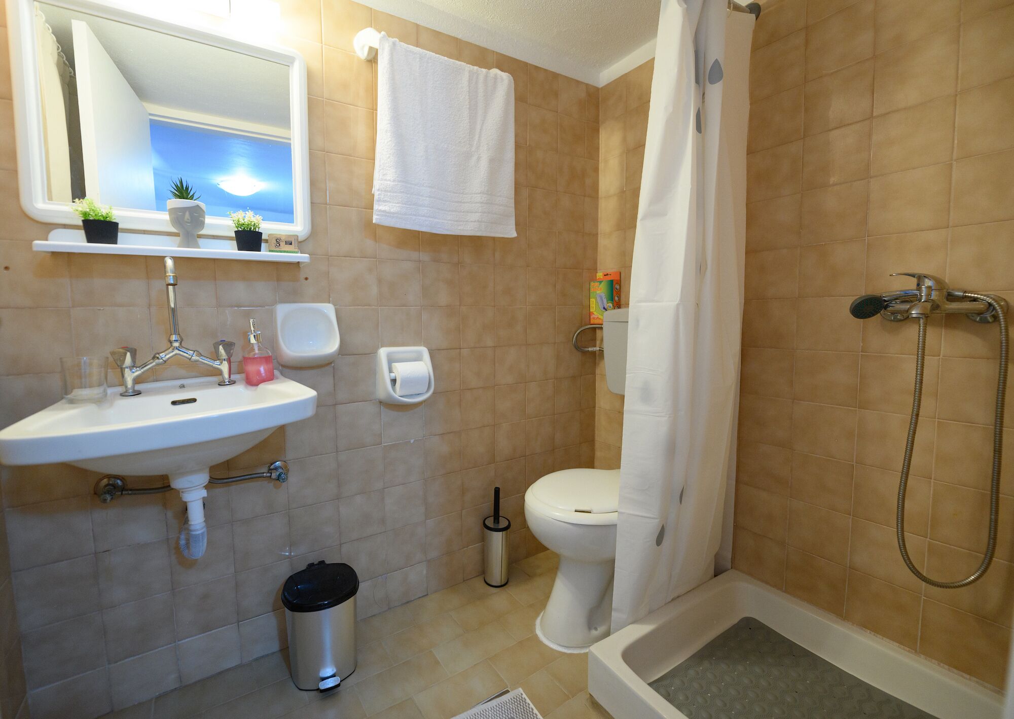 Ein Badezimmer mit Waschbecken, Spiegel, Toilette, Dusche und einem kleinen Mülleimer.