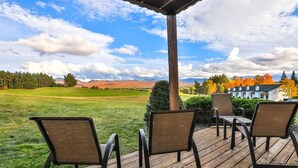 Una terraza de madera con cuatro sillas y una mesa, con vistas a un campo cubierto de césped y una casa con follaje otoñal.