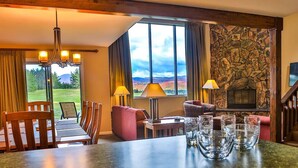 Una habitación acogedora con chimenea de piedra, un comedor con mesa y sillas, y un amplio ventanal con vistas al exterior.