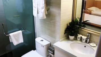 A modern bathroom with a glass shower enclosure, a toilet, a sink with a mirror, and a potted plant.