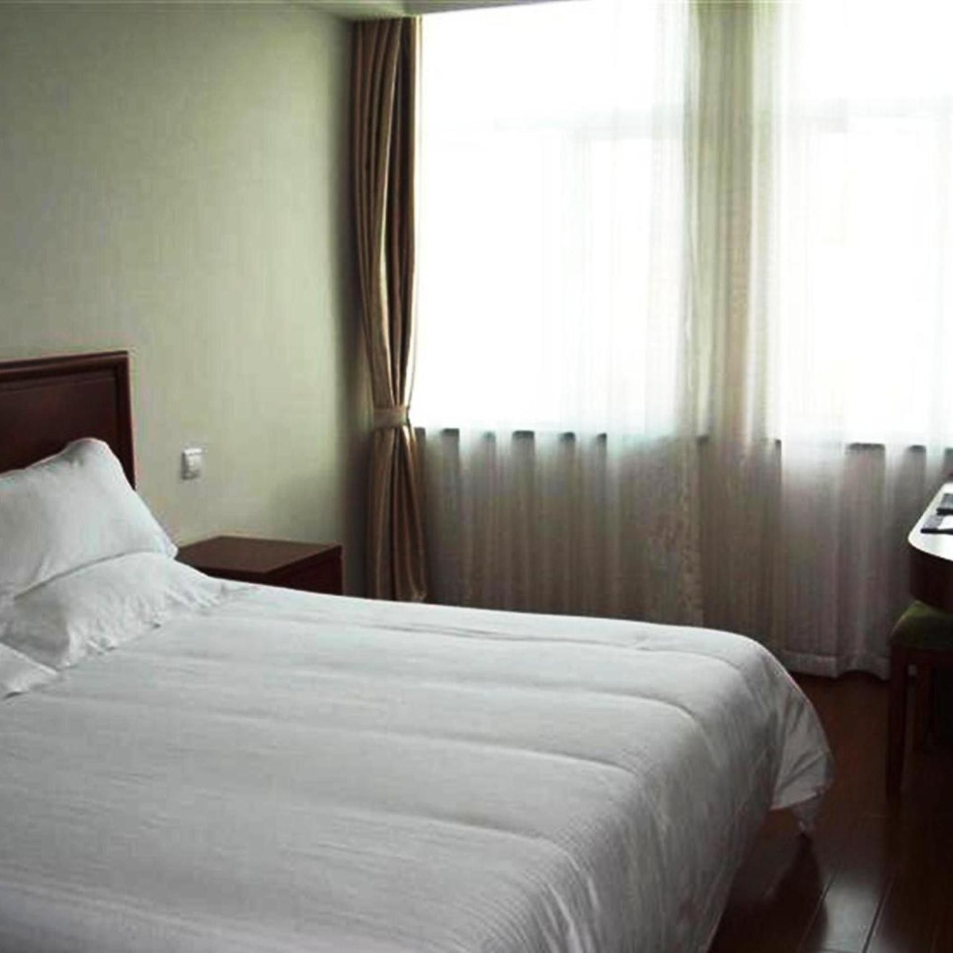 A hotel room with a bed, a nightstand, a window with curtains, and a small table.