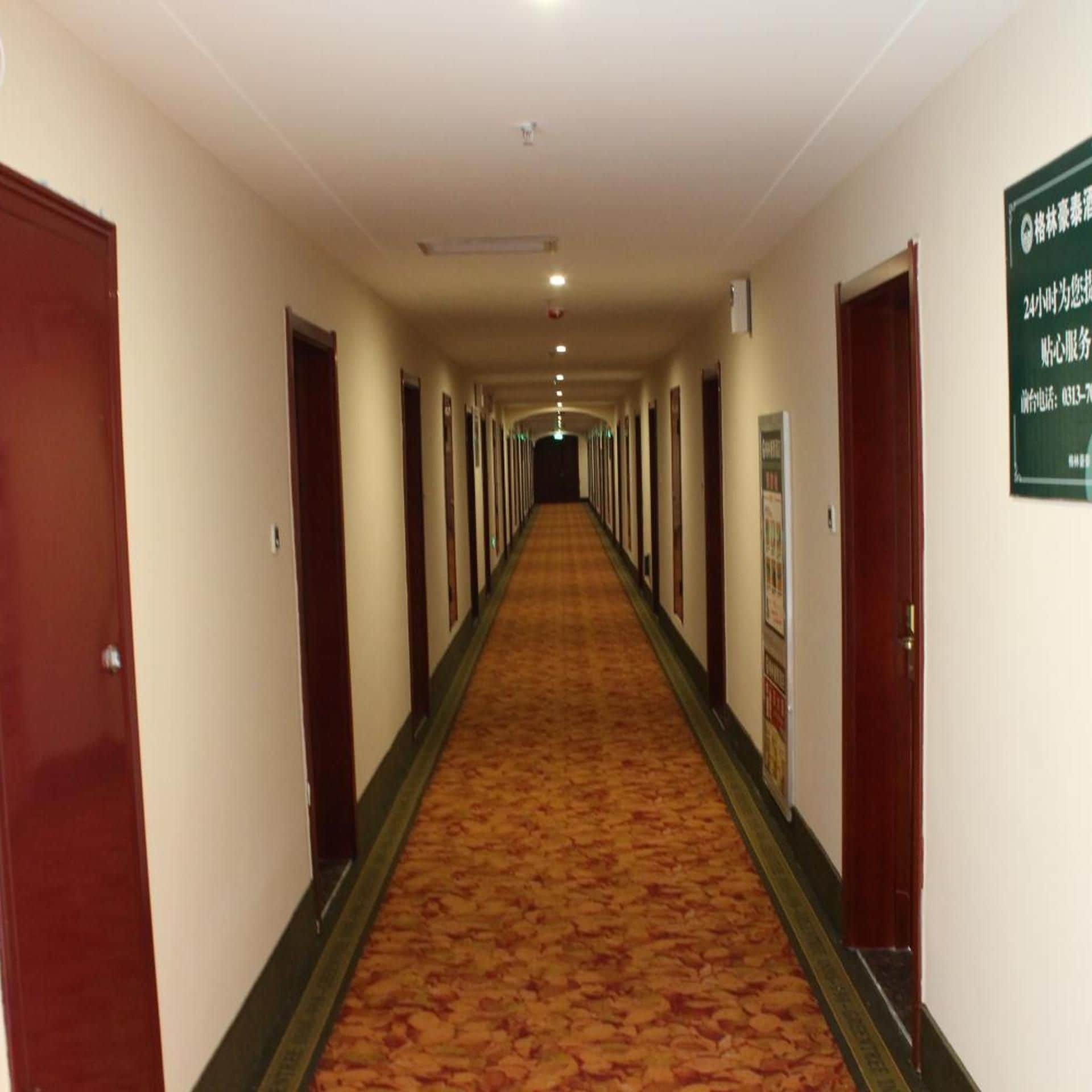 Ein Hotelgang mit Türen an beiden Seiten, einem Teppichboden und einem Schild an der rechten Wand.