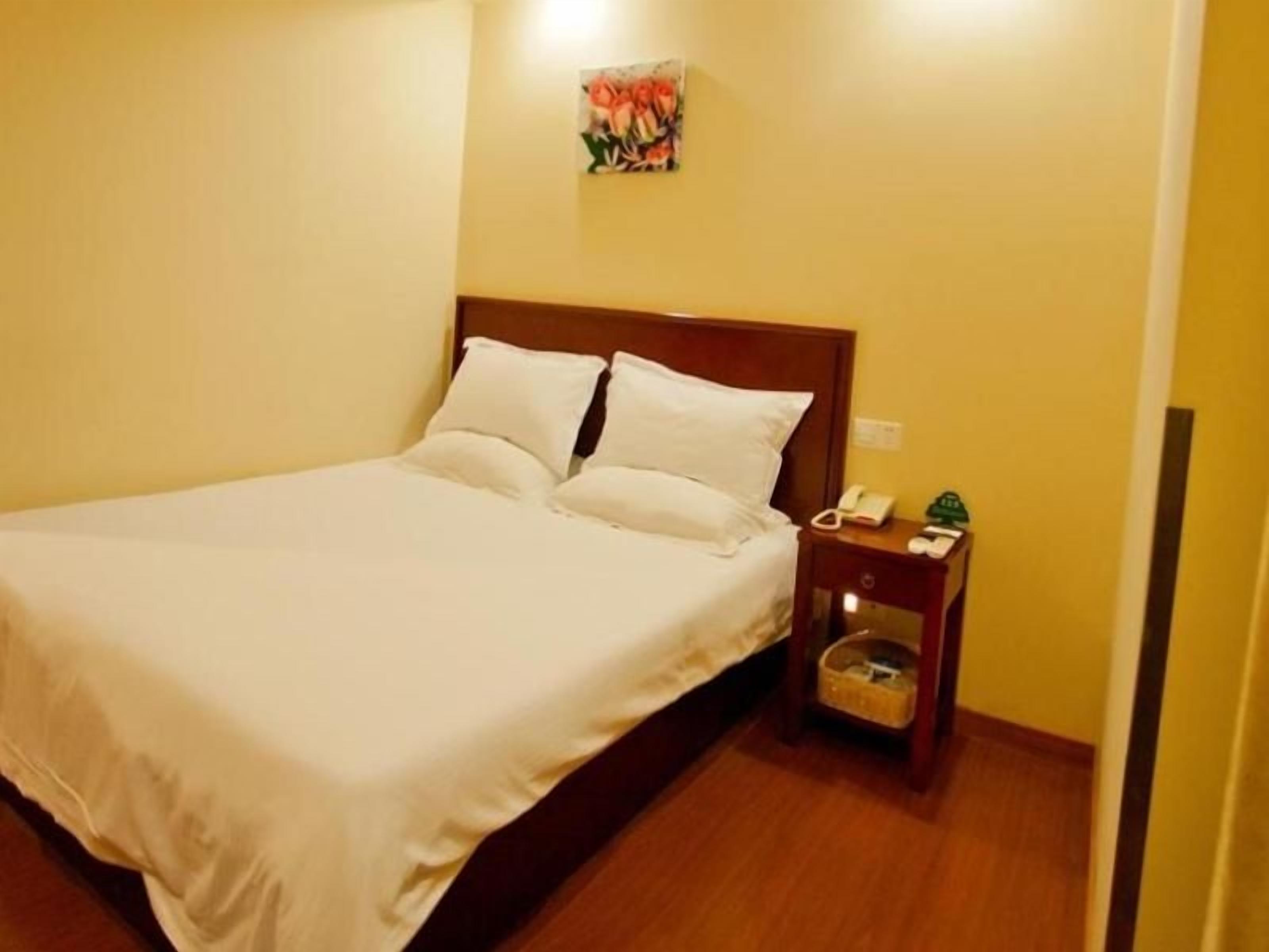 Una cama bien hecha con sábanas blancas en una habitación con piso de madera y una mesita de noche pequeña con lámpara y teléfono.