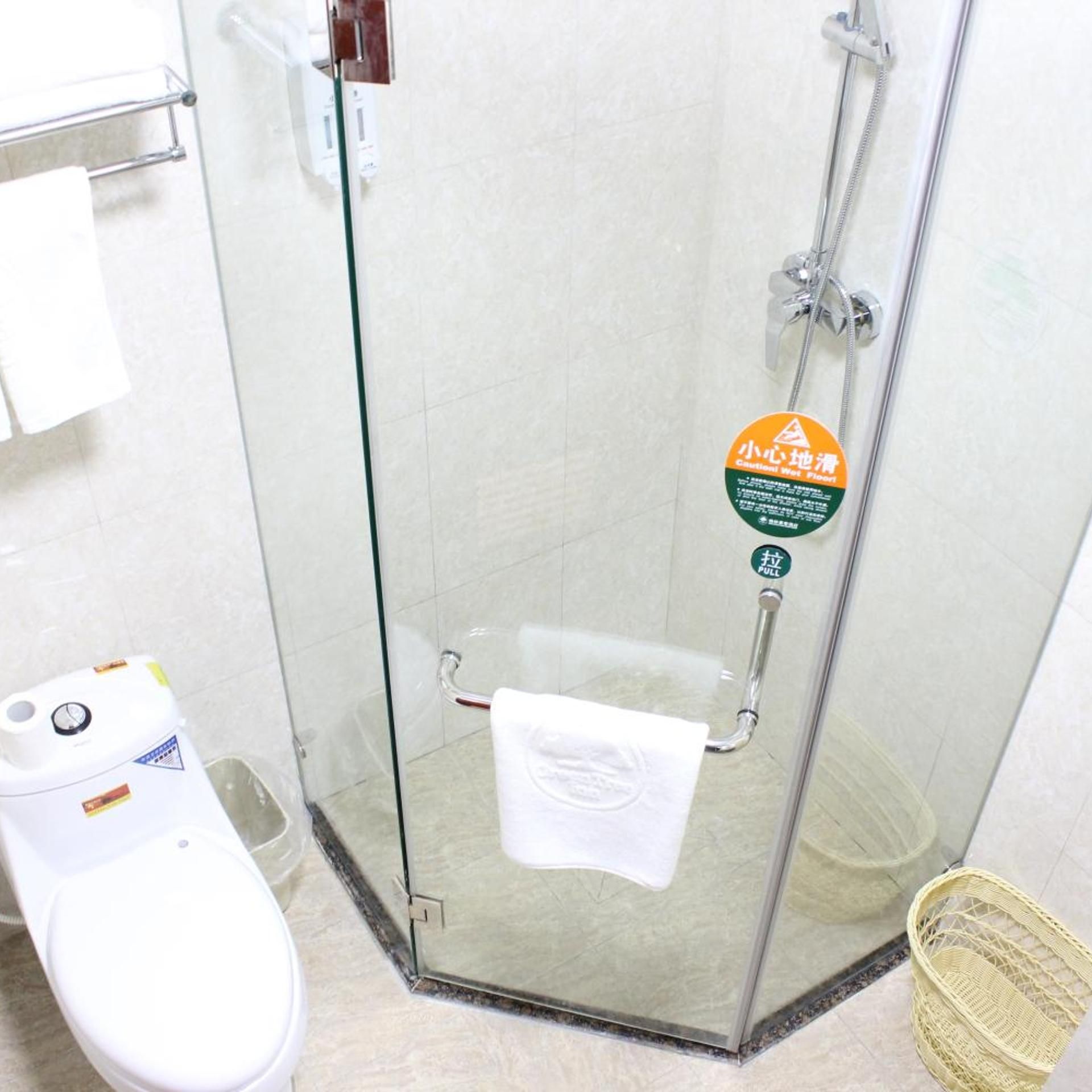 Un baño con cabina de ducha de vidrio, inodoro y un cubo de basura.