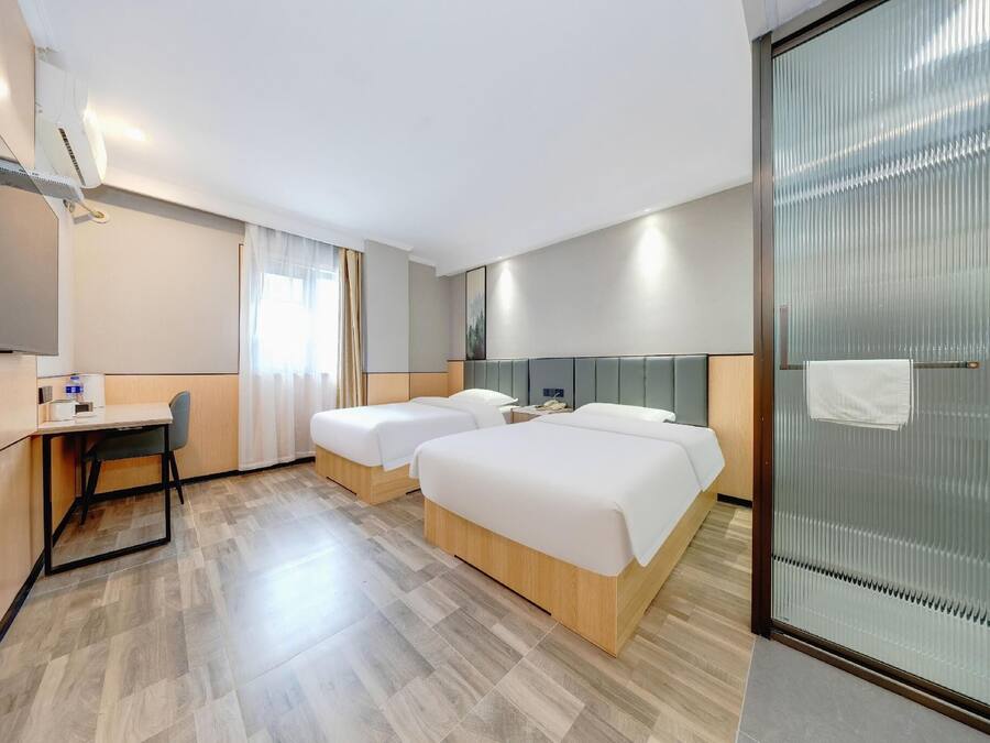 A hotel room with two beds, a desk, a chair, a TV, and a glass partition.