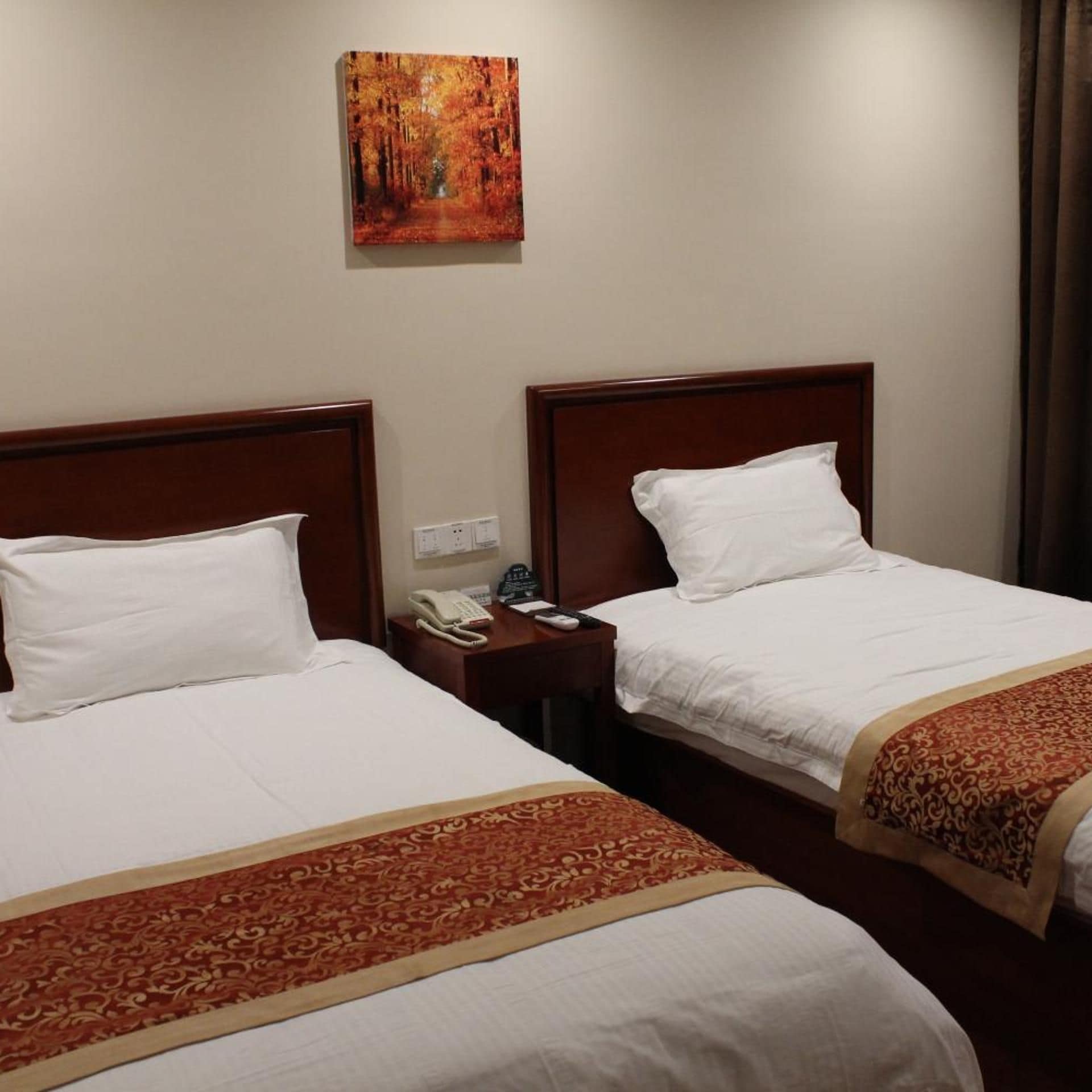 A hotel room with two beds, each with white linens and a brown headboard. There is a painting on the wall above the beds.