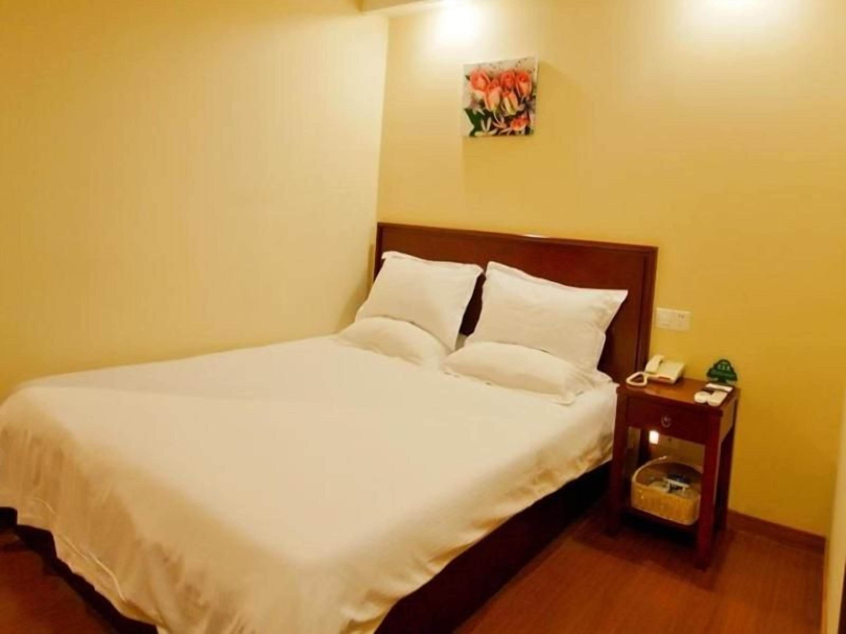 Uma cama de solteiro com cabeceira de madeira, mesa de cabeceira com abajur e telefone fixado na parede.