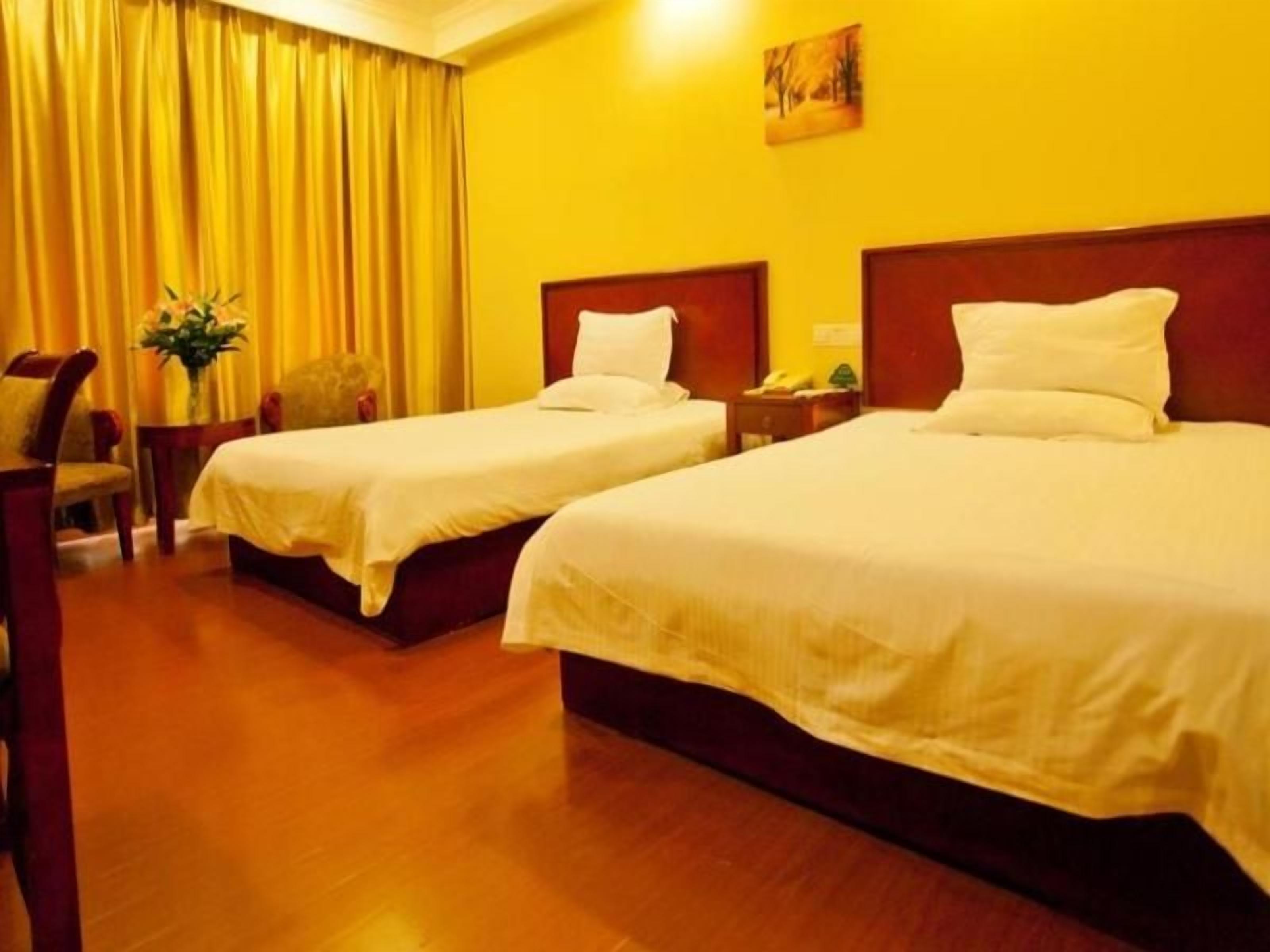 Habitación de hotel con dos camas, piso de madera, pared amarilla y un cuadro.