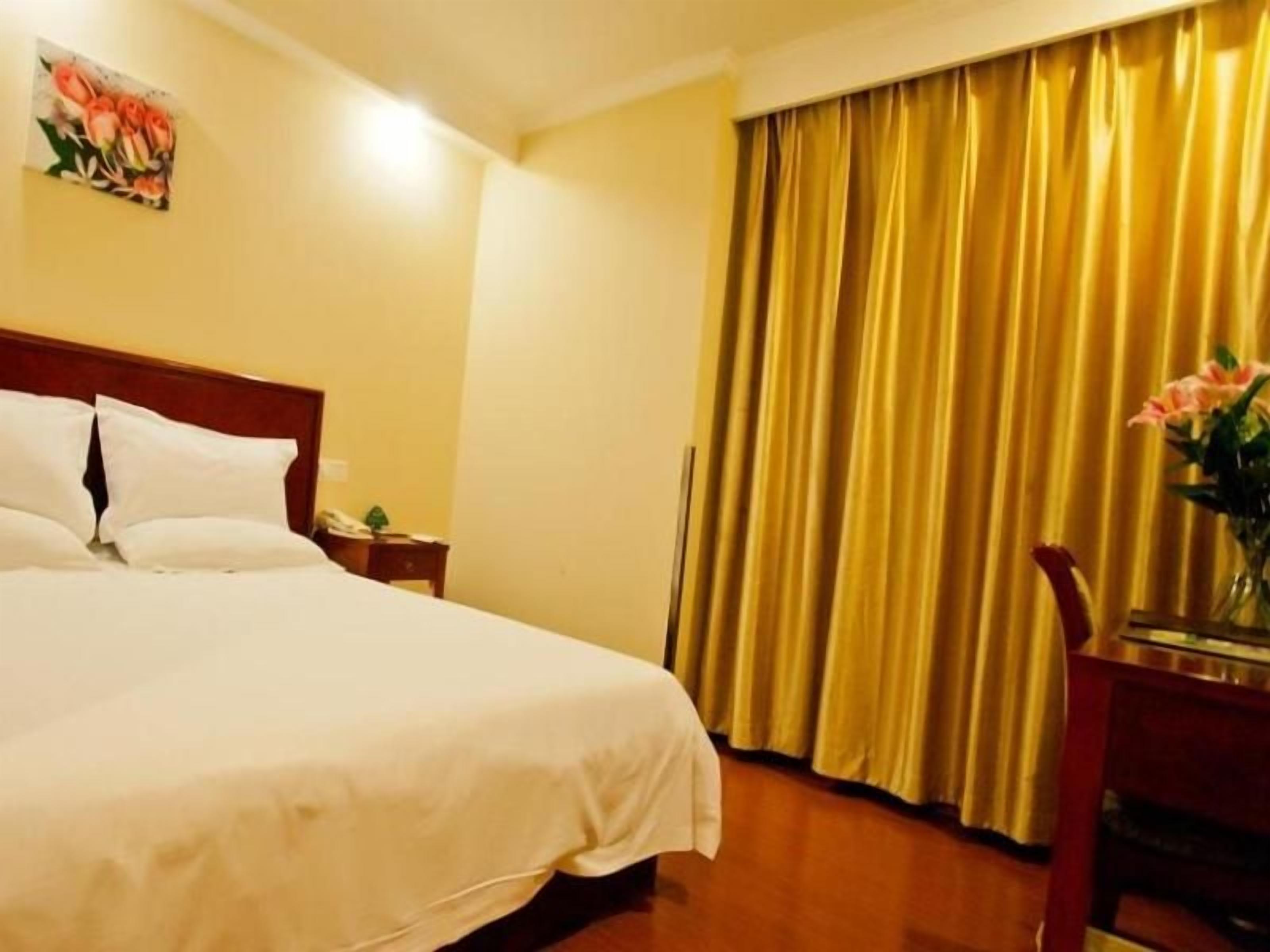 A hotel room with a large bed, a nightstand, a desk with a chair, and a window with curtains.