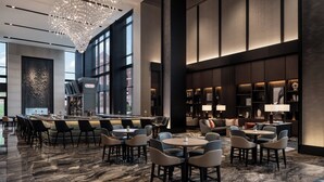 A modern hotel lobby with a bar area, seating arrangements, and a large chandelier.