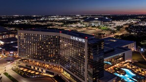A modern hotel with a prominent "LOEW'S" sign, featuring a curved facade, multiple floors, and a well-lit entrance area.