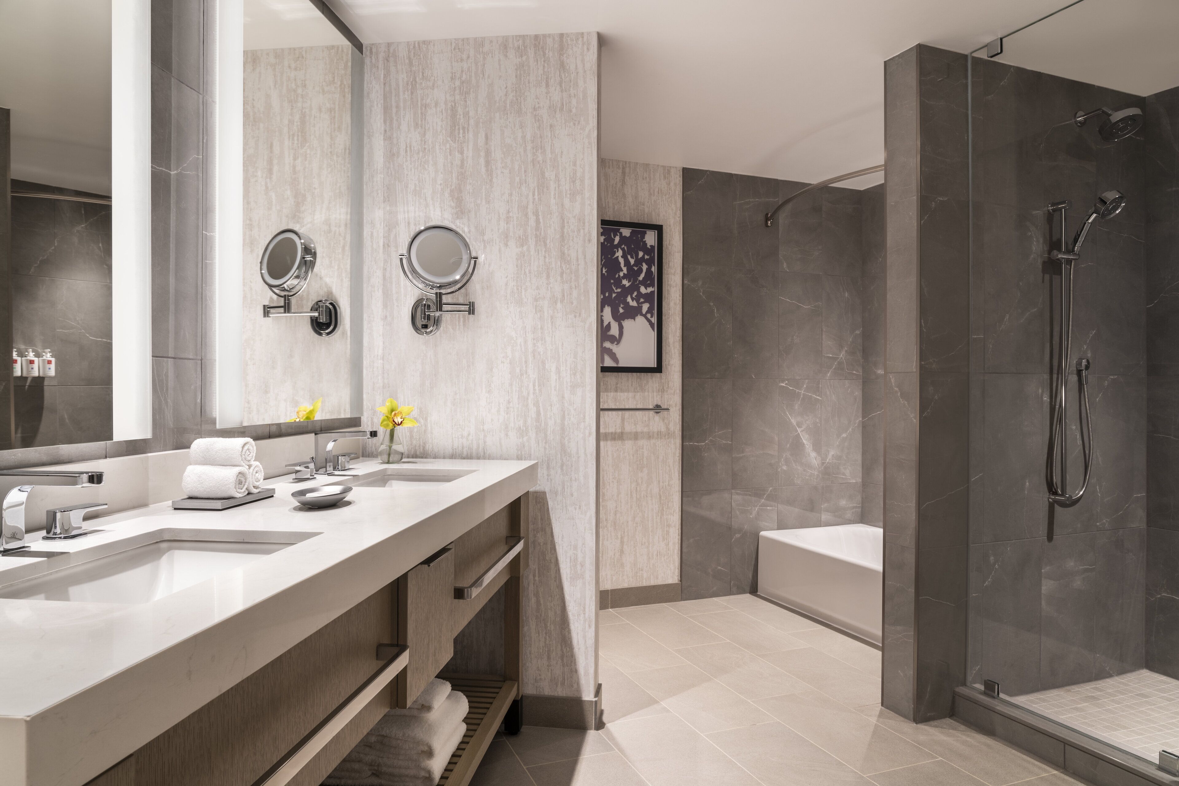 A modern bathroom with two sinks, a large mirror, and a walk-in shower.