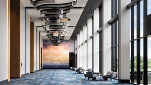 A modern hotel lobby with a blue carpet, a unique ceiling light fixture, and large windows offering a view. - Loews Arlington (Arlington)