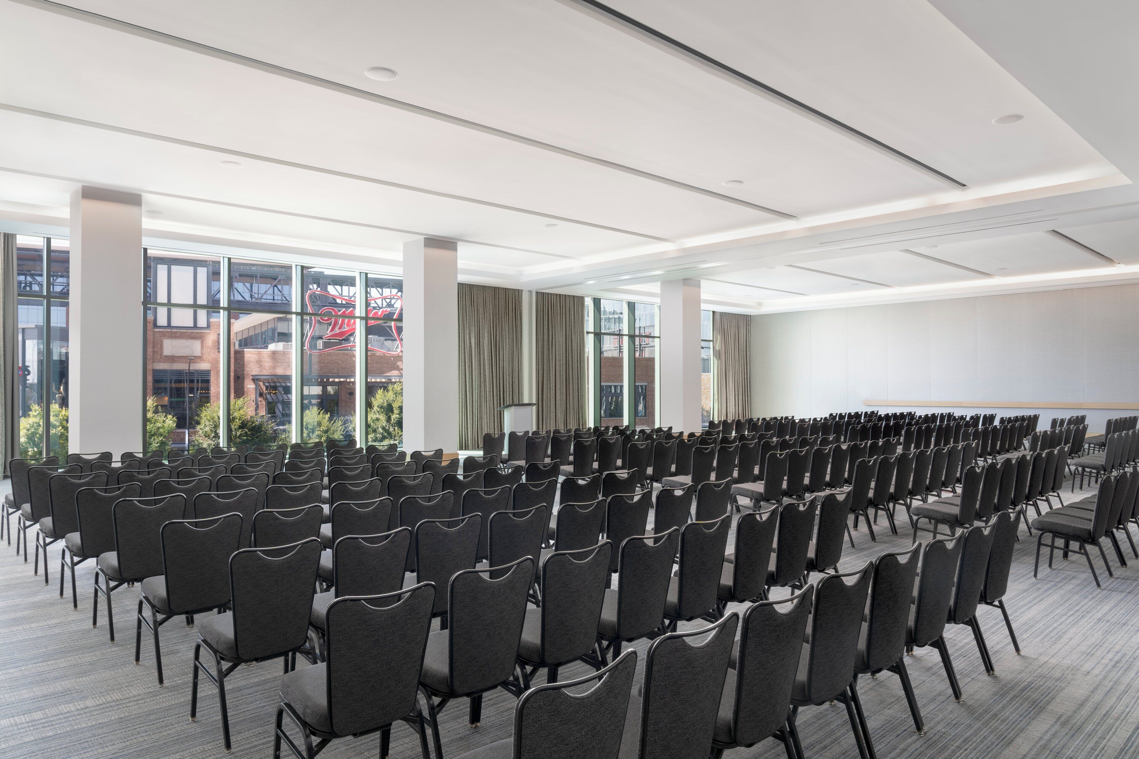 Uma sala de conferências com fileiras de cadeiras, janelas amplas e um quadro branco.