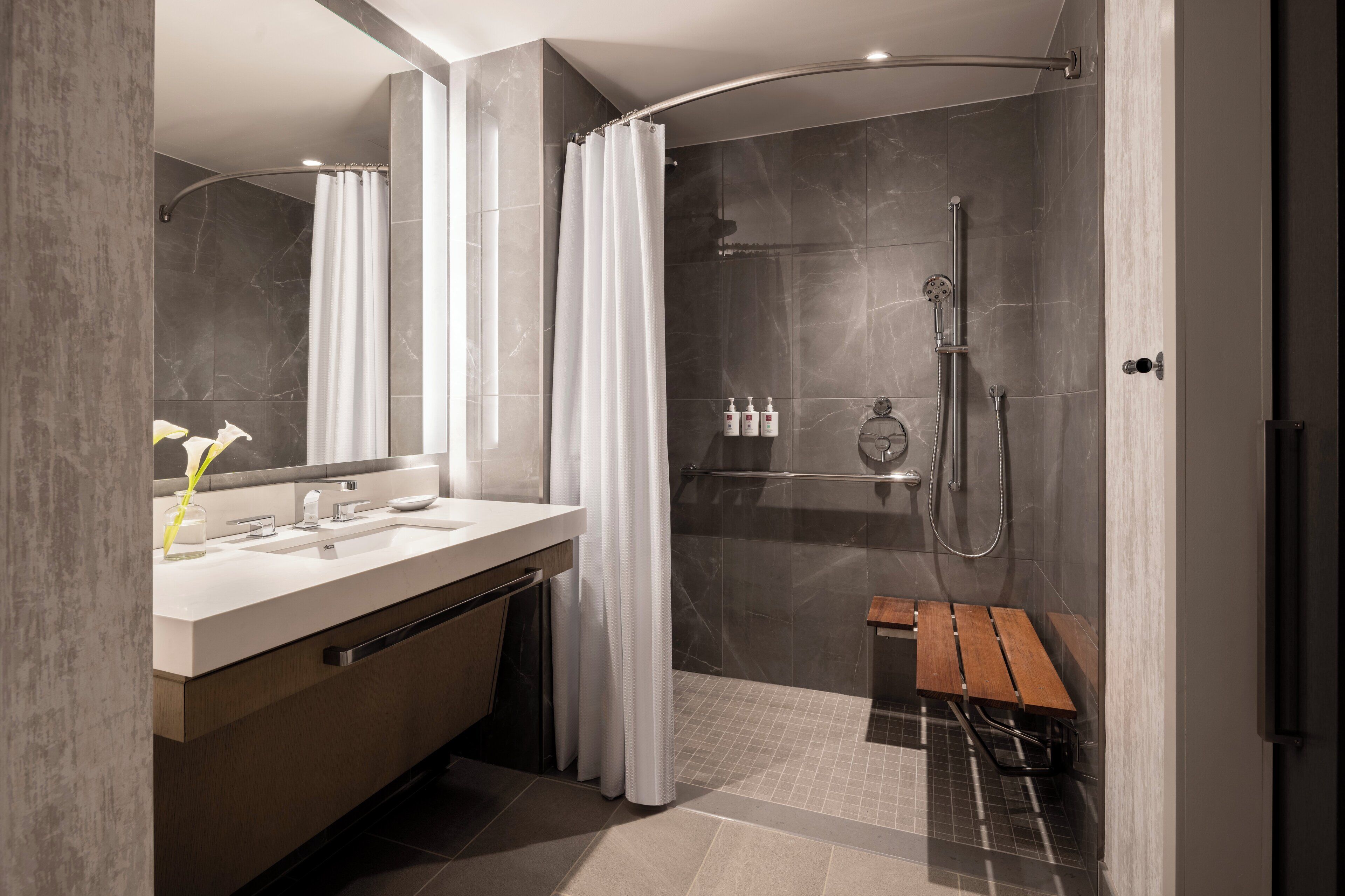 A modern bathroom with a shower, vanity, and a bench.