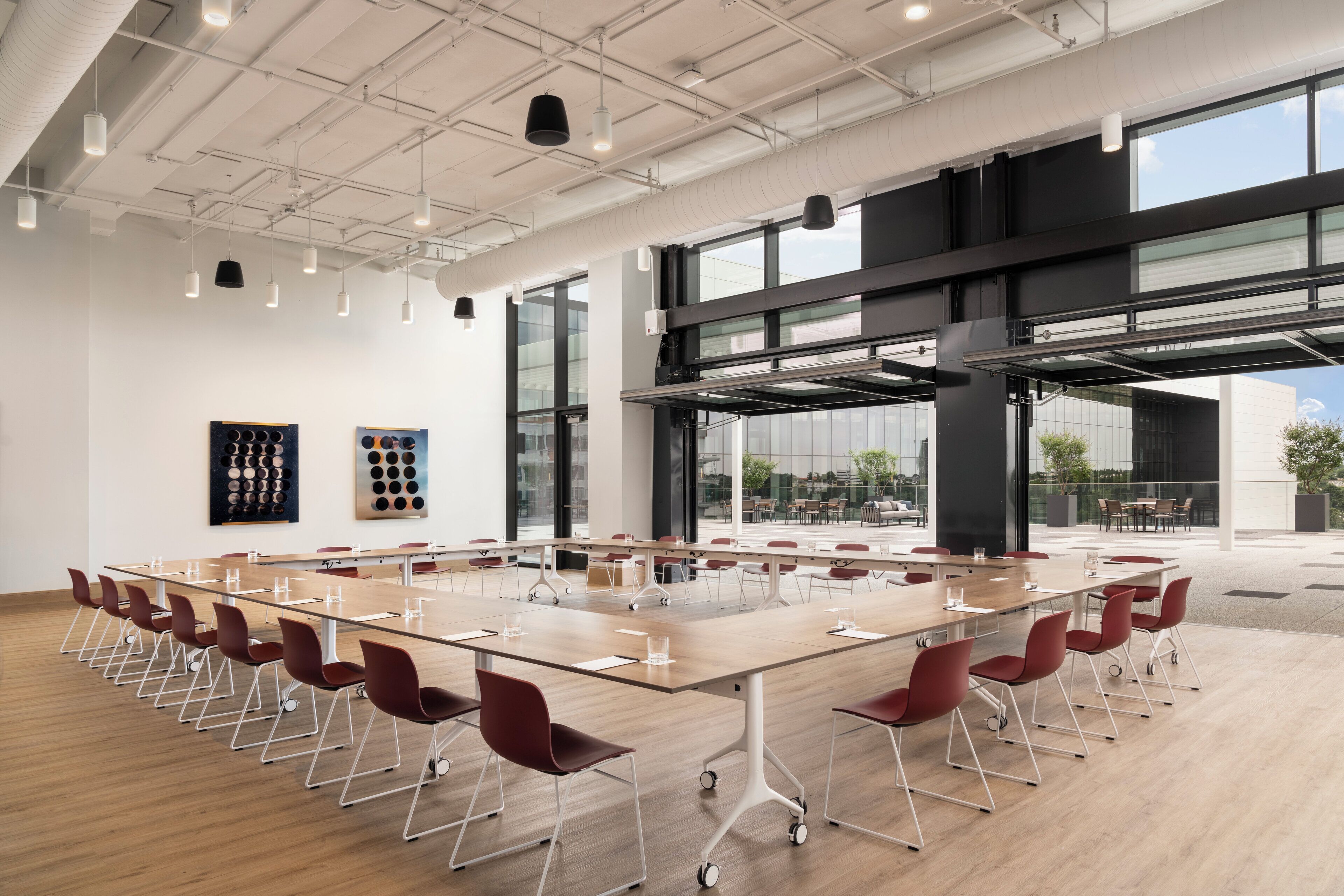 A conference room with a long table, red chairs, and large windows.