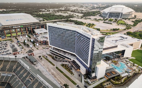 A modern hotel with a prominent glass facade, a rooftop pool, and a parking area.