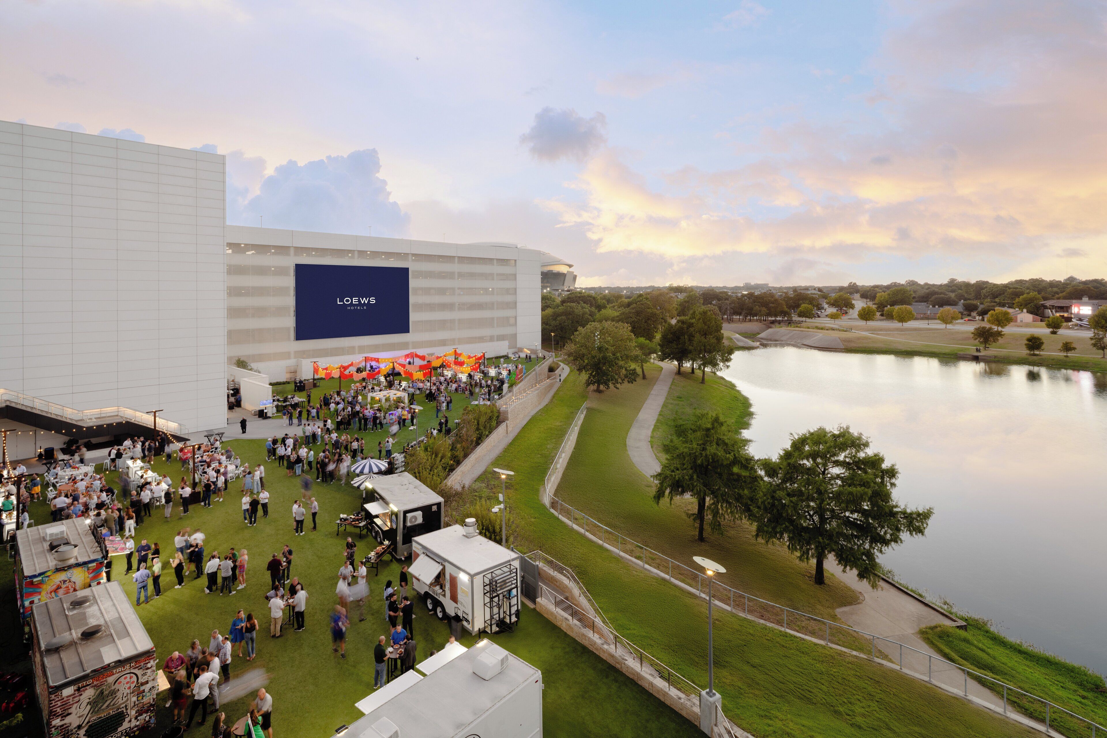 A large building with a prominent LOEWS sign, surrounded by a grassy area and a body of water.