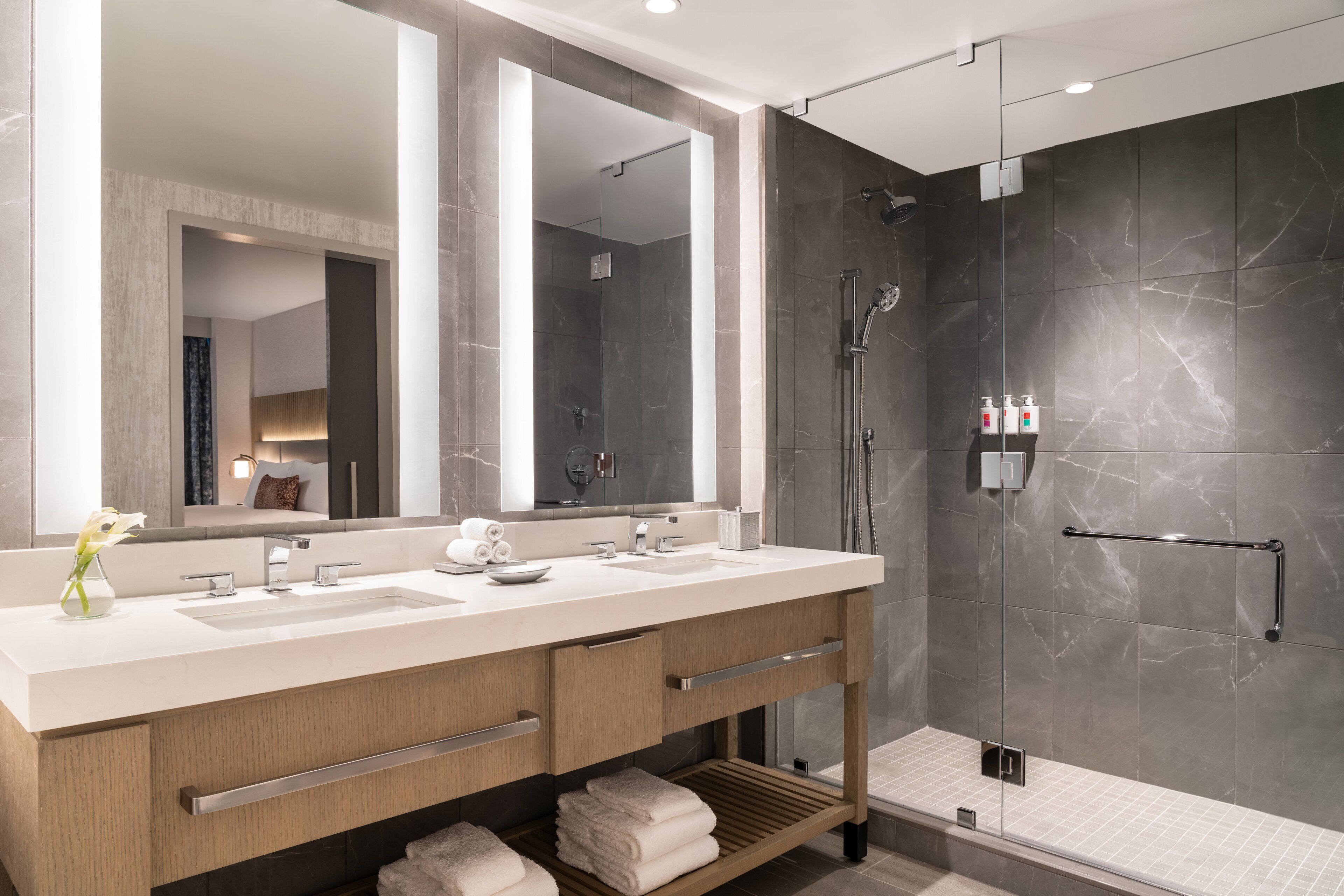 A modern bathroom with a large mirror, two sinks, a shower, and a towel rack.