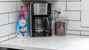 Una cocina con cafetera, un bote de crema para café y un recipiente de vidrio en la encimera.