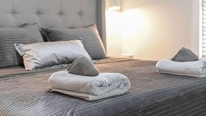 Una cama bien hecha con ropa de cama y almohadas grises, un cabecero capitonado y una lámpara de noche.