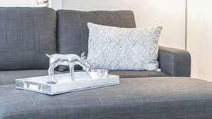 Un sofá gris con un cojín estampado y una bandeja de vidrio transparente con una escultura de metal.