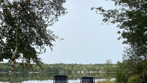 Deux chaises de plage sont placées face à un lac dont le rivage sablonneux est recouvert de feuilles mortes.