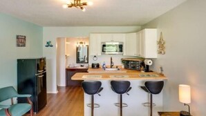 A modern kitchen with white cabinets, a central island with bar stools, a microwave, and a refrigerator.