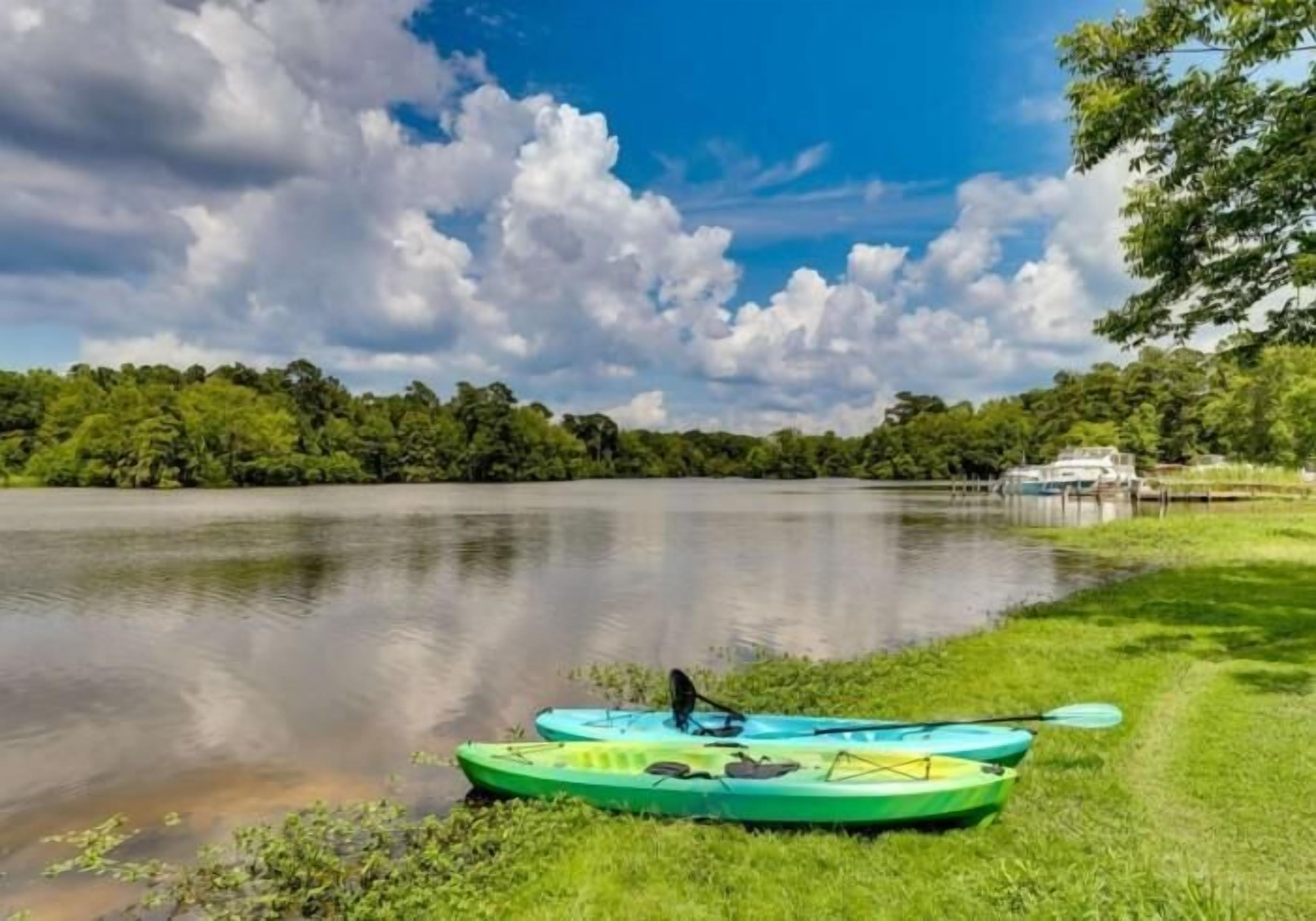 A calm lake with kayaks on the grassy shore and a dock in the background.