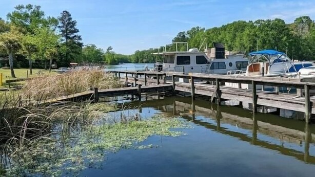 A docked RV and a boat at a calm lake with wooden walkways and surrounding greenery.