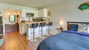 A compact hotel room with a kitchenette, a bed with a blue cover, and a wall-mounted fish decoration.