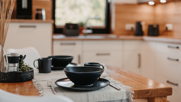 Une cuisine moderne avec une table en bois, des bols noirs et une machine à café.