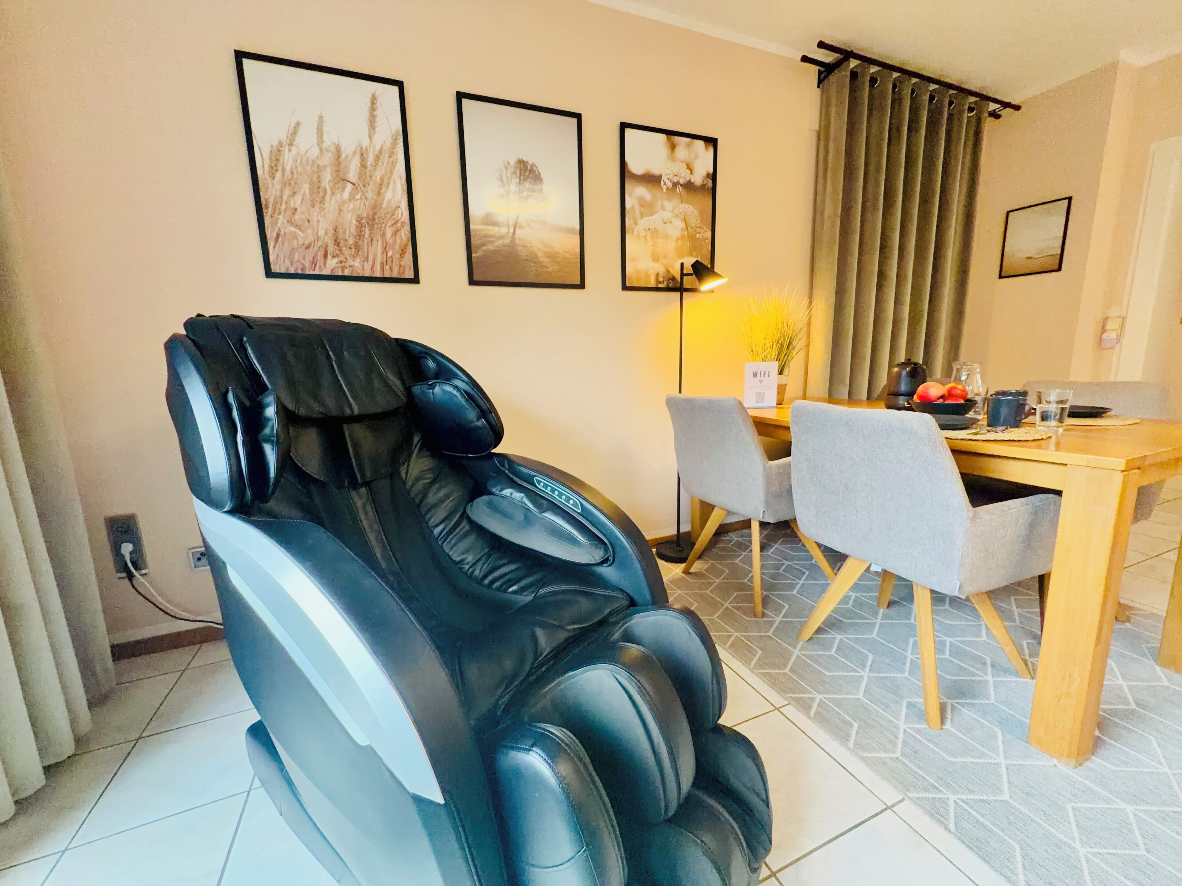 Una silla de masaje, una mesa de comedor con sillas y tres cuadros en la pared.