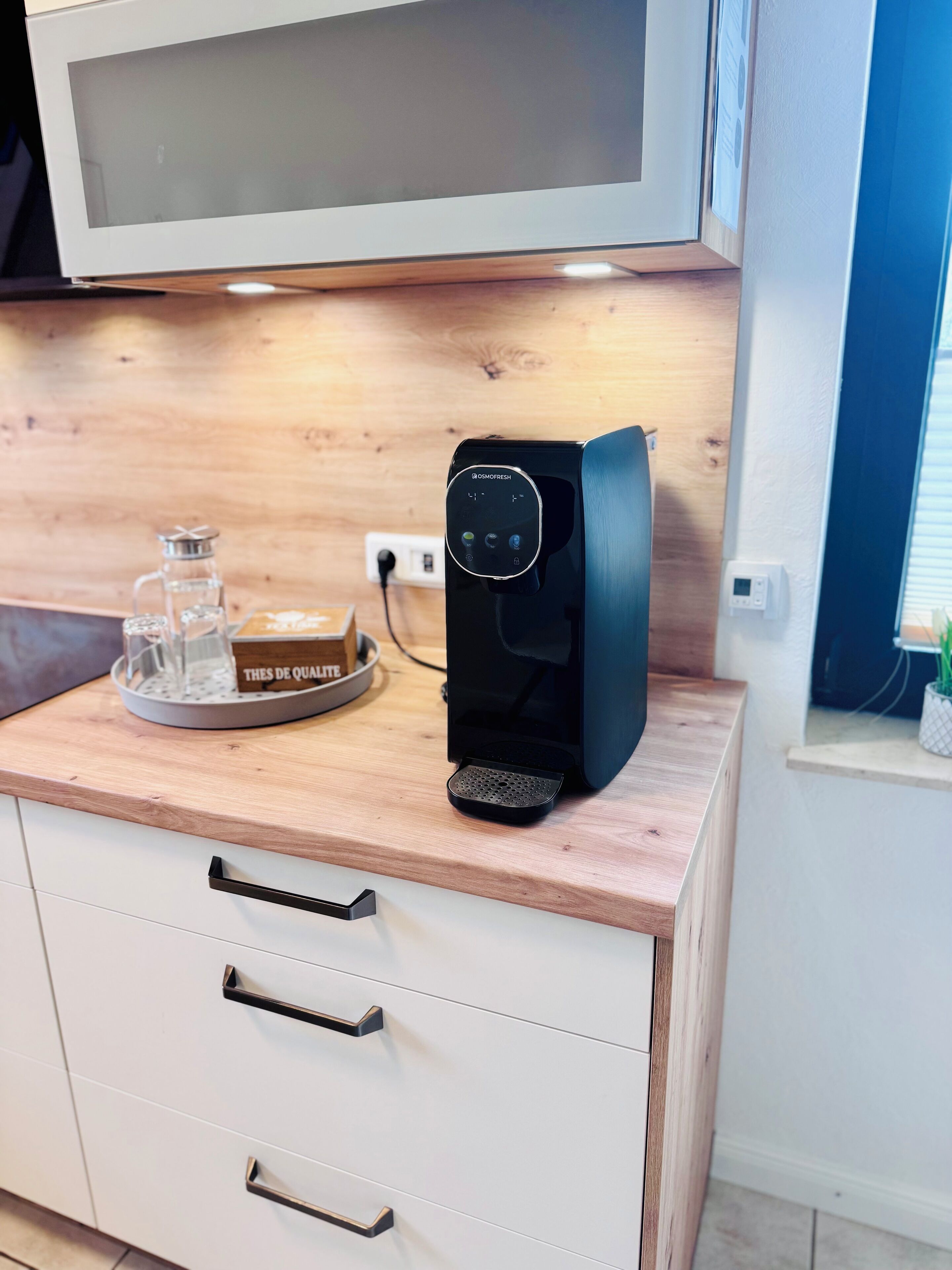 A kitchenette with a coffee machine, a microwave, and a small tray with a glass container and a box labeled "THES DE QUATRE".