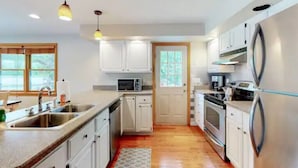 Une cuisine moderne avec des armoires blanches, des appareils en acier inoxydable et des luminaires suspendus.
