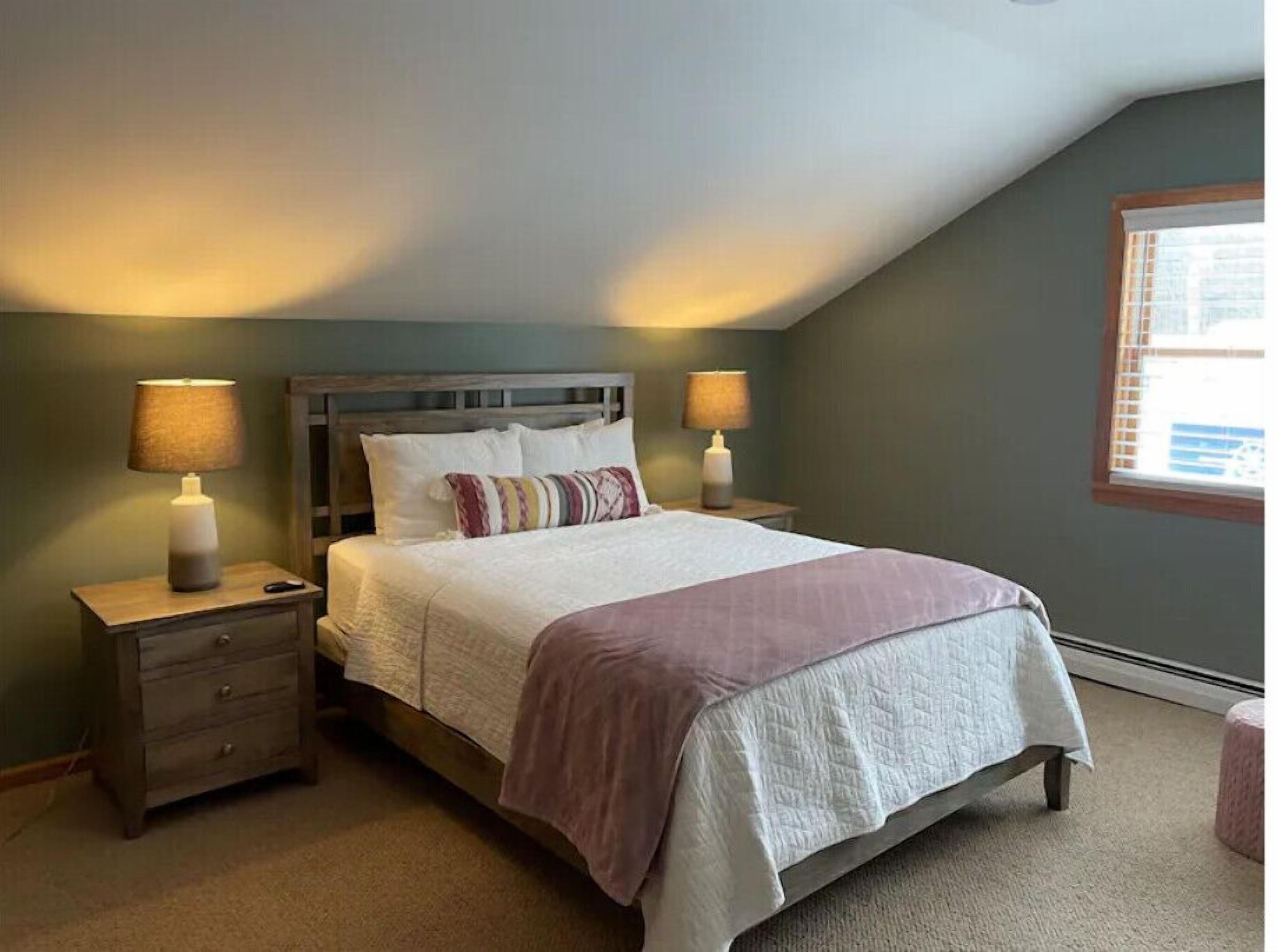 Quarto com cama, duas mesas de cabeceira, um criado-mudo, janela e vista para o exterior.