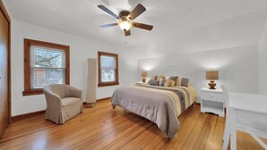 Ein Schlafzimmer mit Bett, Sessel, Schreibtisch und Deckenventilator.