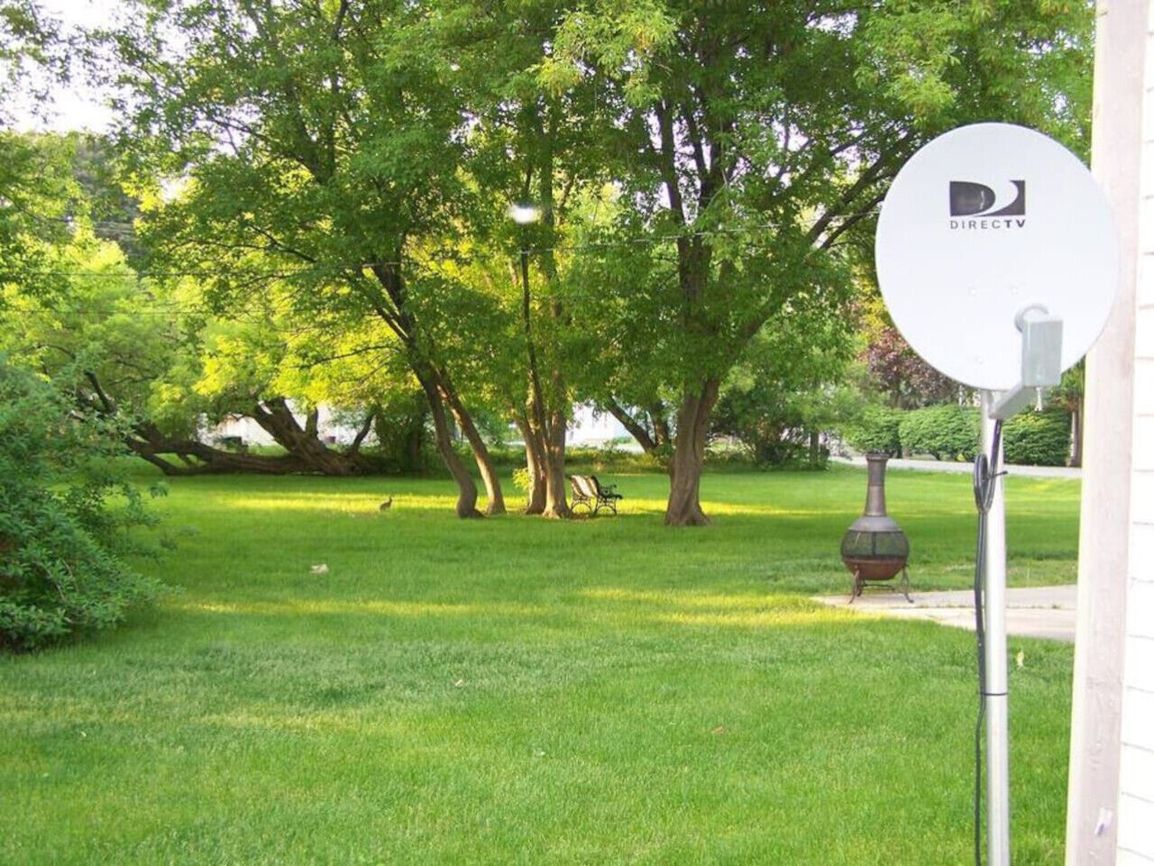 A park with a grassy area, trees, a bench, and a satellite dish.