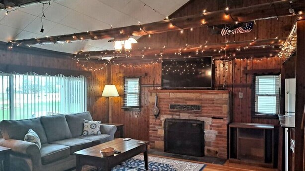 A cozy living room with a fireplace, wooden walls, and string lights. - Rustic Retreat Cottage sleeps 6 with a lake view! (Worth Township)