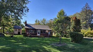 A two-story house with a porch, surrounded by a well-maintained lawn and trees. - Rustic Retreat Cottage sleeps 6 with a lake view! (Worth Township)