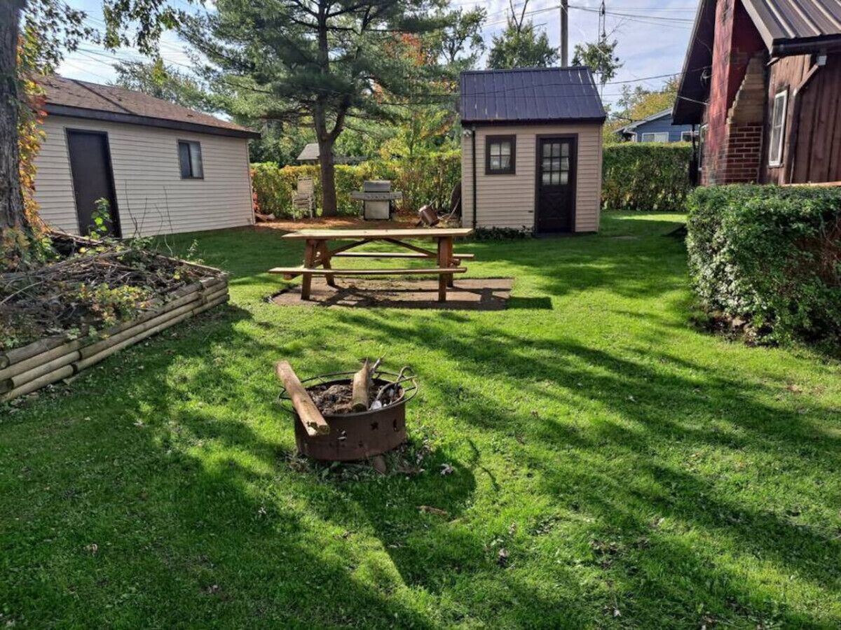 Ein Garten mit einem Holztisch, einer Feuerstelle und zwei kleinen Hütten.