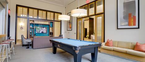 Une table de billard dans une pièce spacieuse, avec un canapé et des tabourets de bar.