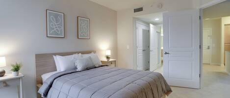A bedroom with a bed, bedside tables, and a door leading to another room.