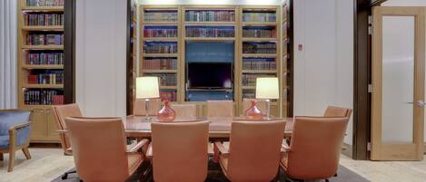 A conference room with a long table, six chairs, two lamps, and a bookshelf in the background.
