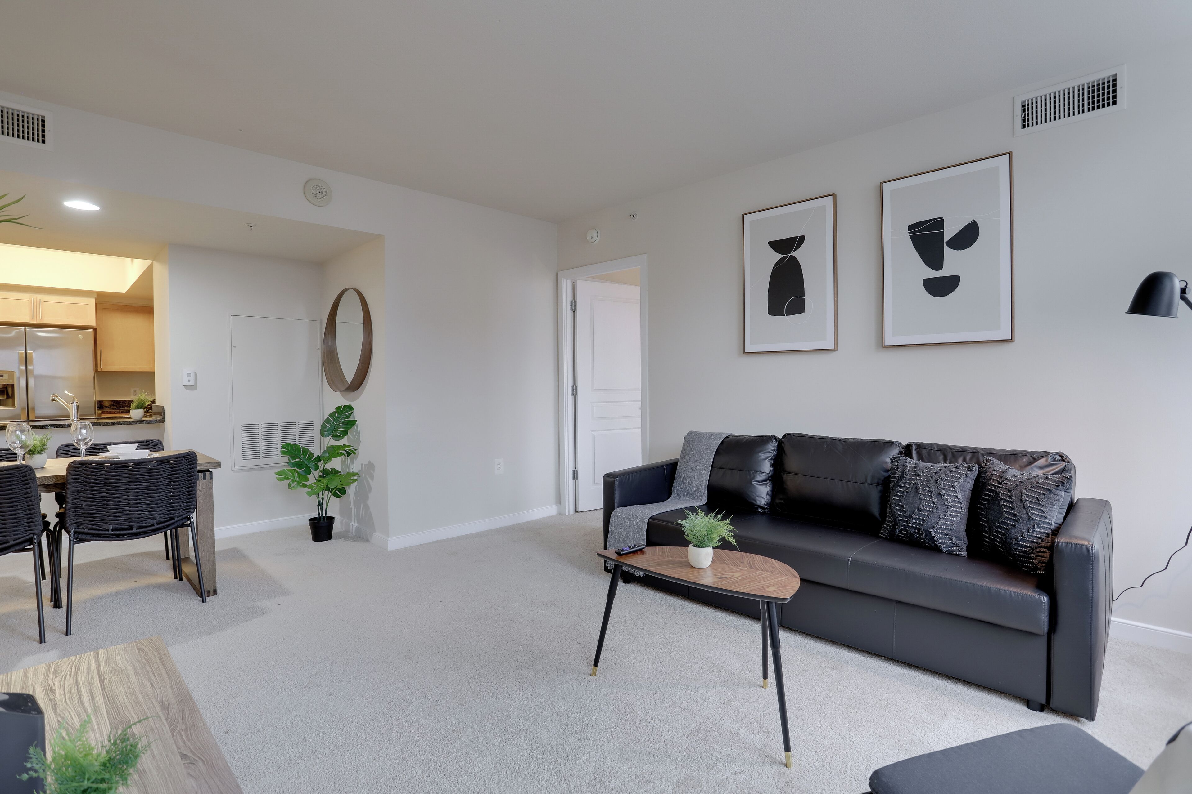 A modern living room with a black leather sofa, a coffee table, and a dining area with a table and chairs.
